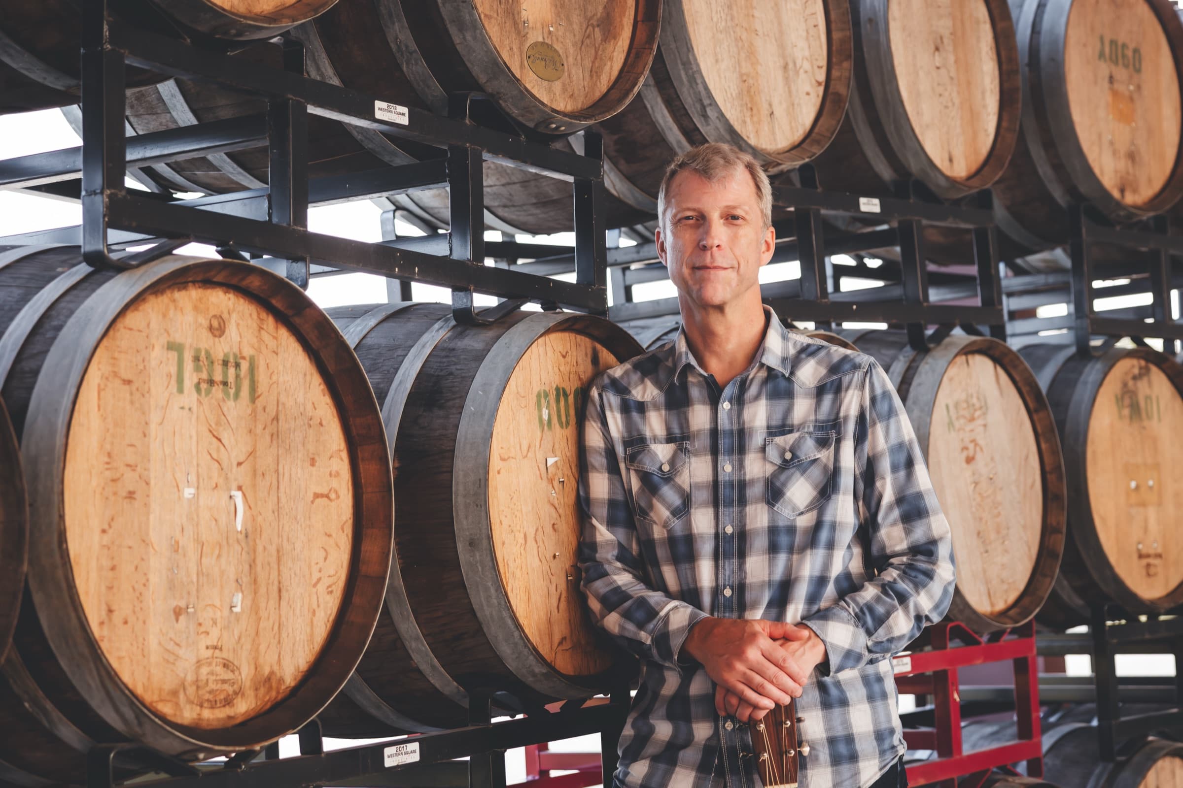 Ian leaning against a rack of oak barrels