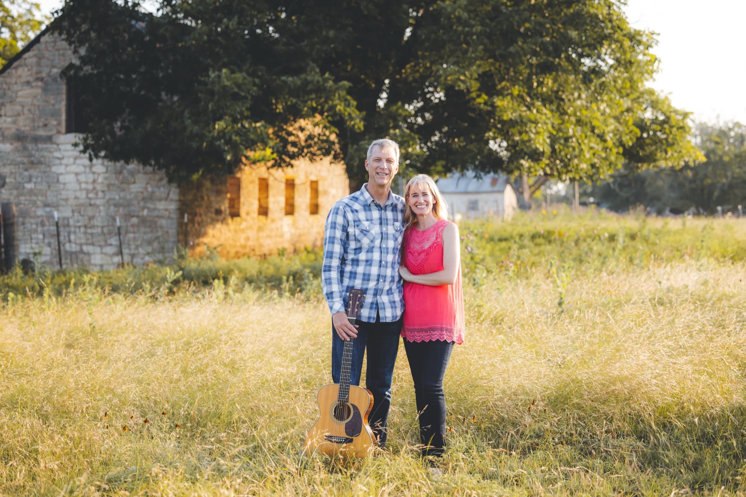 Ian and a companion standing in tall grass by a stone barn, guitar at his feet